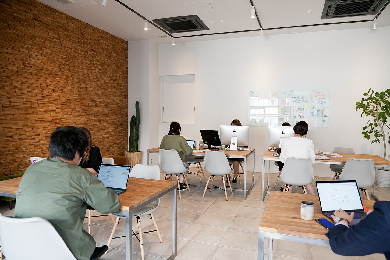 A bright open-plan office with a timber feature wall, where people work on laptops at shared wooden tables